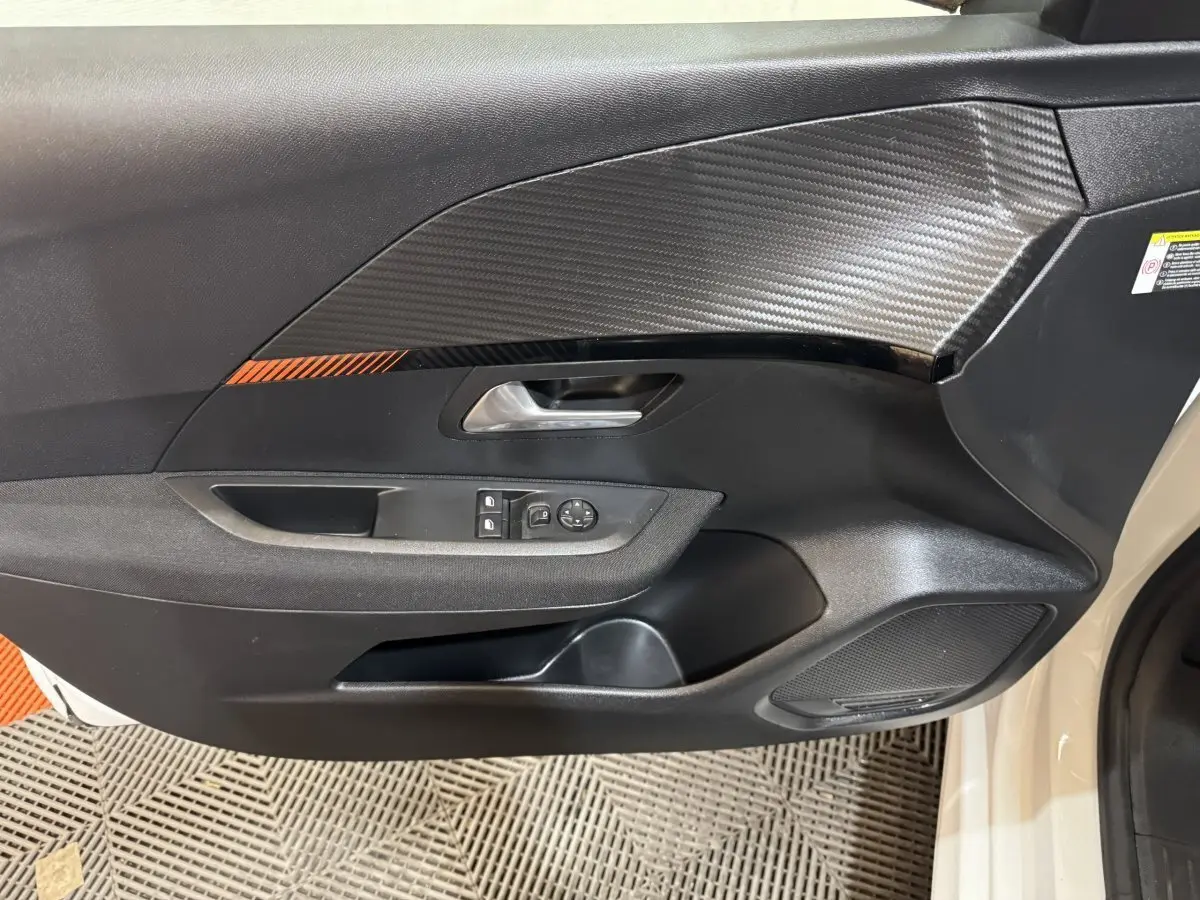 Vue rapprochée de la porte avant gauche noire avec insert effet carbone et commandes des vitres de la Peugeot 208 électrique.