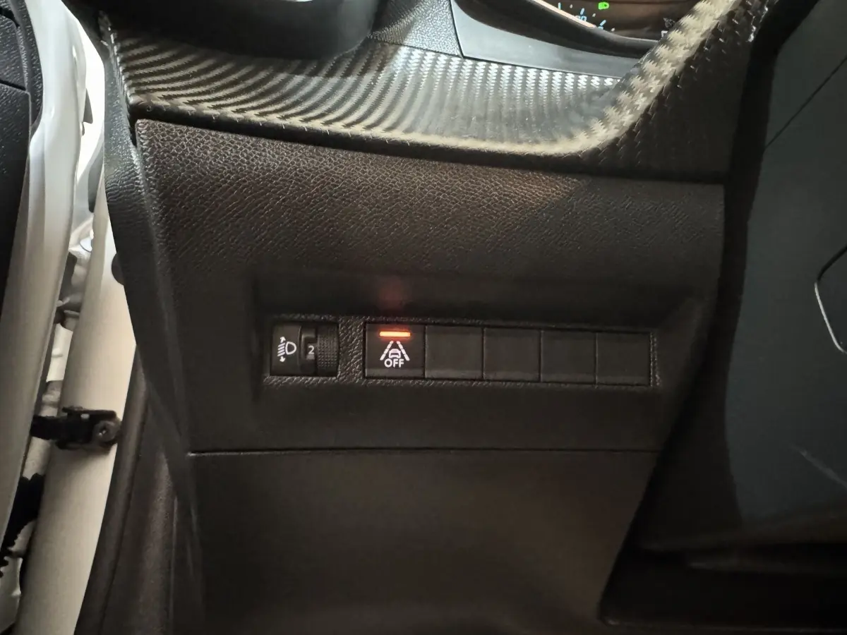 Gros plan sur les commandes noires du tableau de bord côté gauche d’une Peugeot 208 électrique, bouton d’aide à la conduite désactivé.