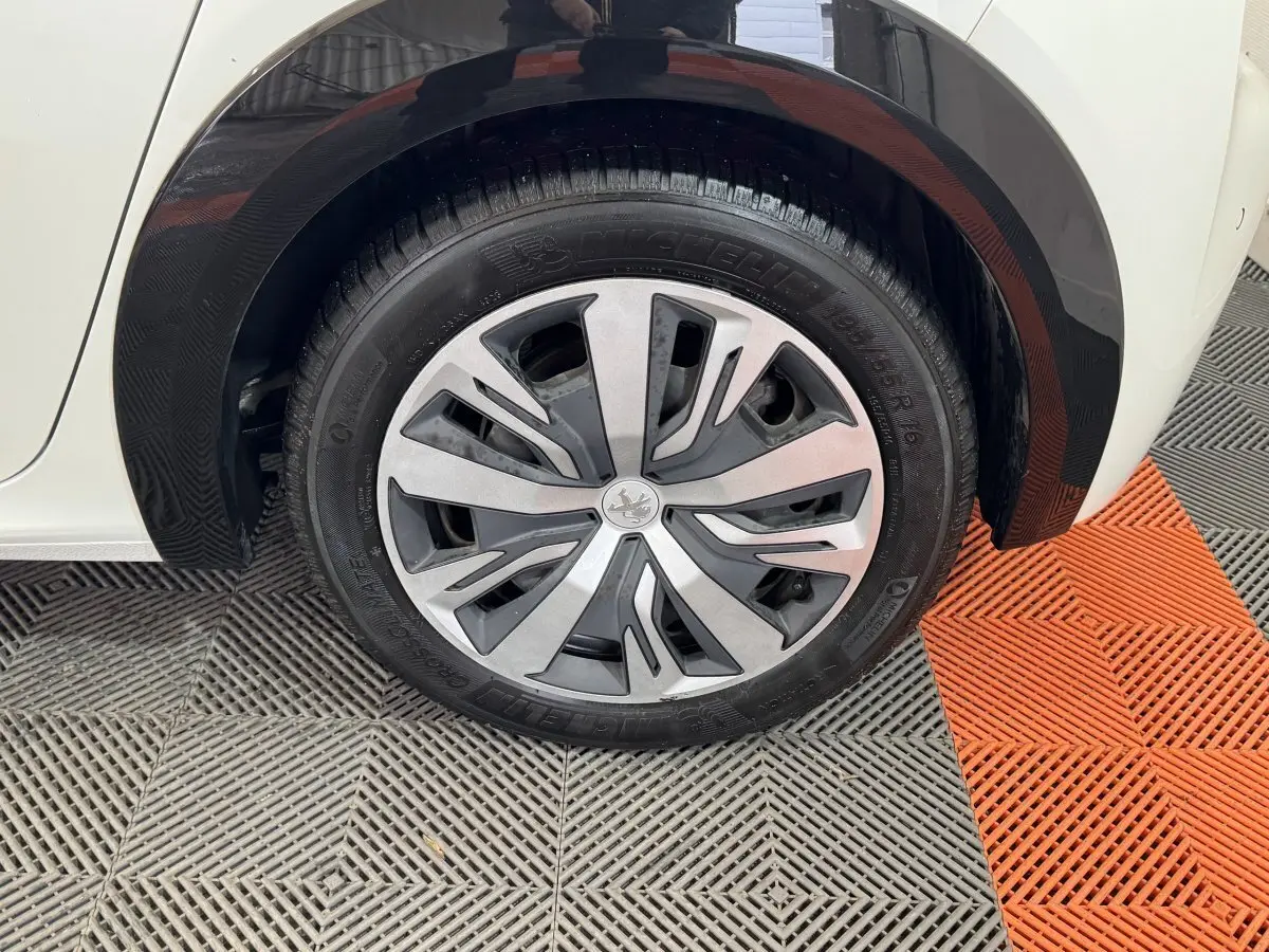 Gros plan sur la roue arrière droite d'une Peugeot 208 électrique blanche avec jante aluminium et passage de roue noir.