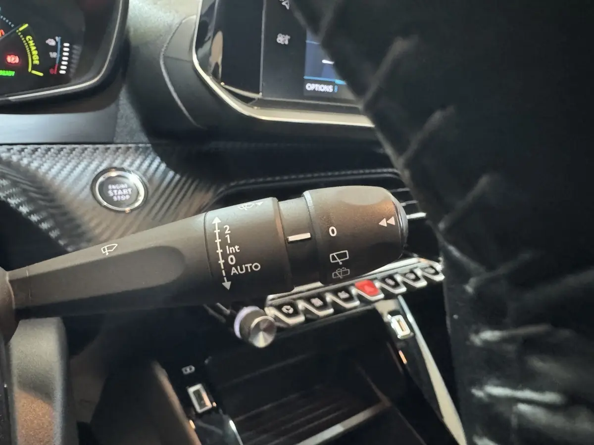 Gros plan sur la commande d’essuie-glace et bouton démarrage dans l’habitacle noir d’une Peugeot 208 électrique.