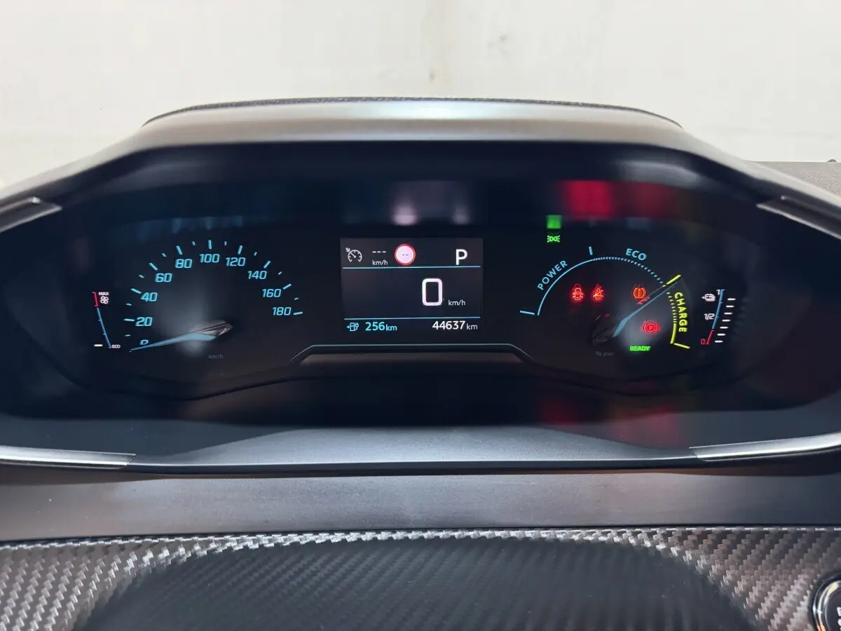 Tableau de bord numérique de Peugeot 208 électrique, affichage central avec vitesse à 0 km/h et jauges colorées.