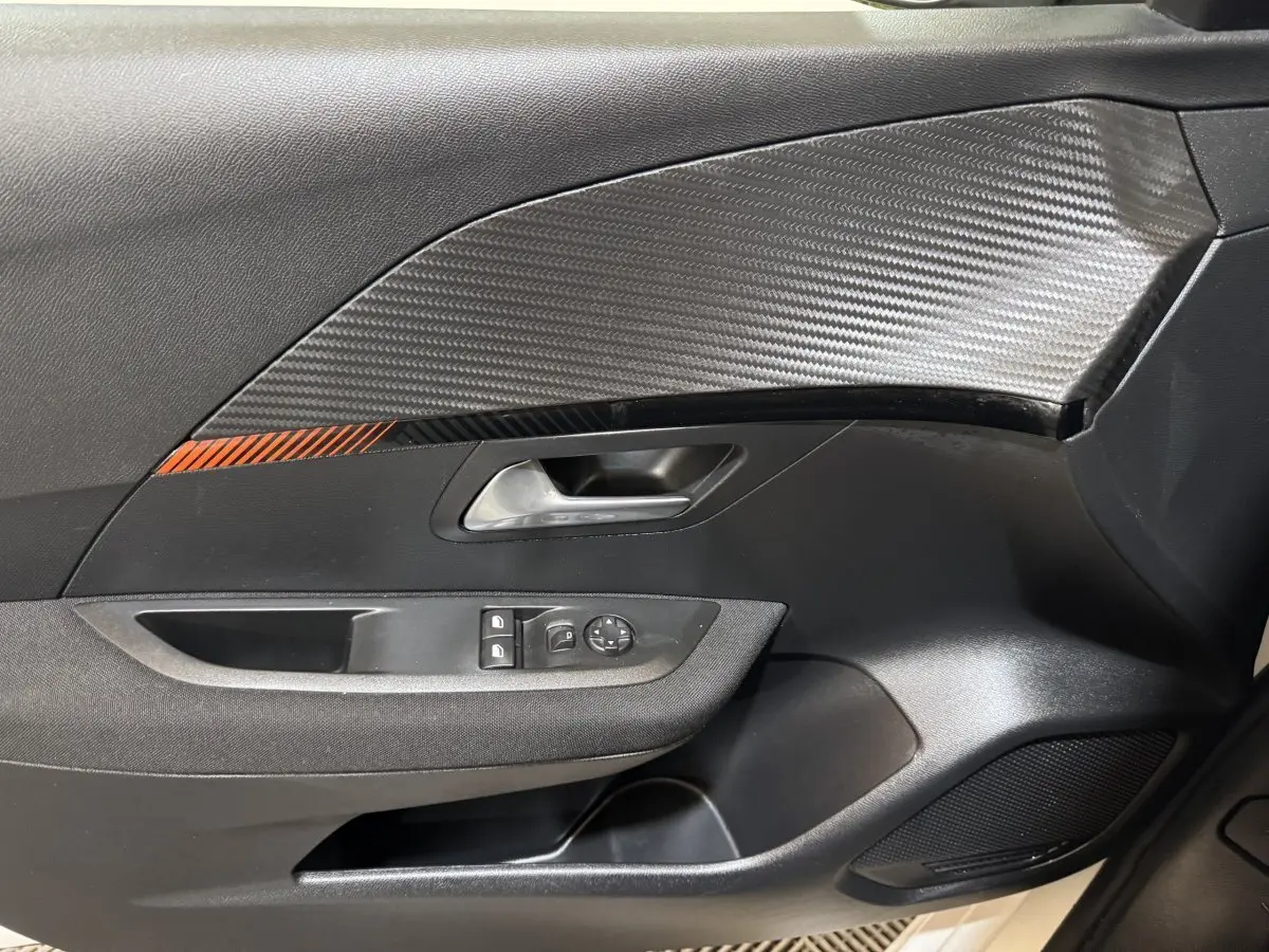 Vue rapprochée de la porte intérieure côté gauche de la Peugeot 208 électrique avec insert carbone et bande orange.