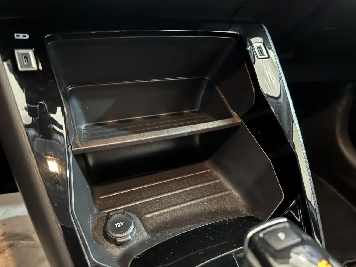 Gros plan sur la console centrale noire de la Peugeot 208 électrique avec prise 12V visible au premier plan.