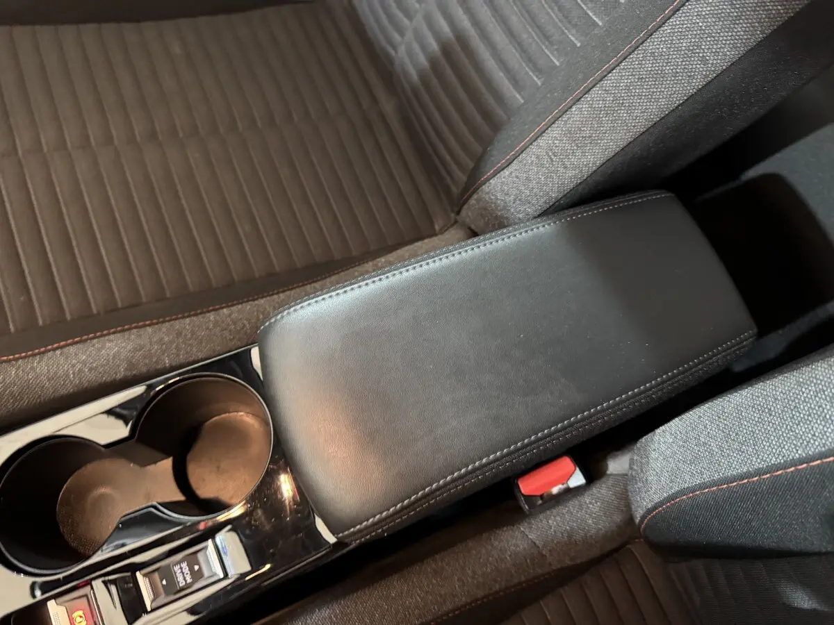 Vue rapprochée de l'accoudoir central noir et des sièges gris avec surpiqûres rouges dans une Peugeot 208 électrique.