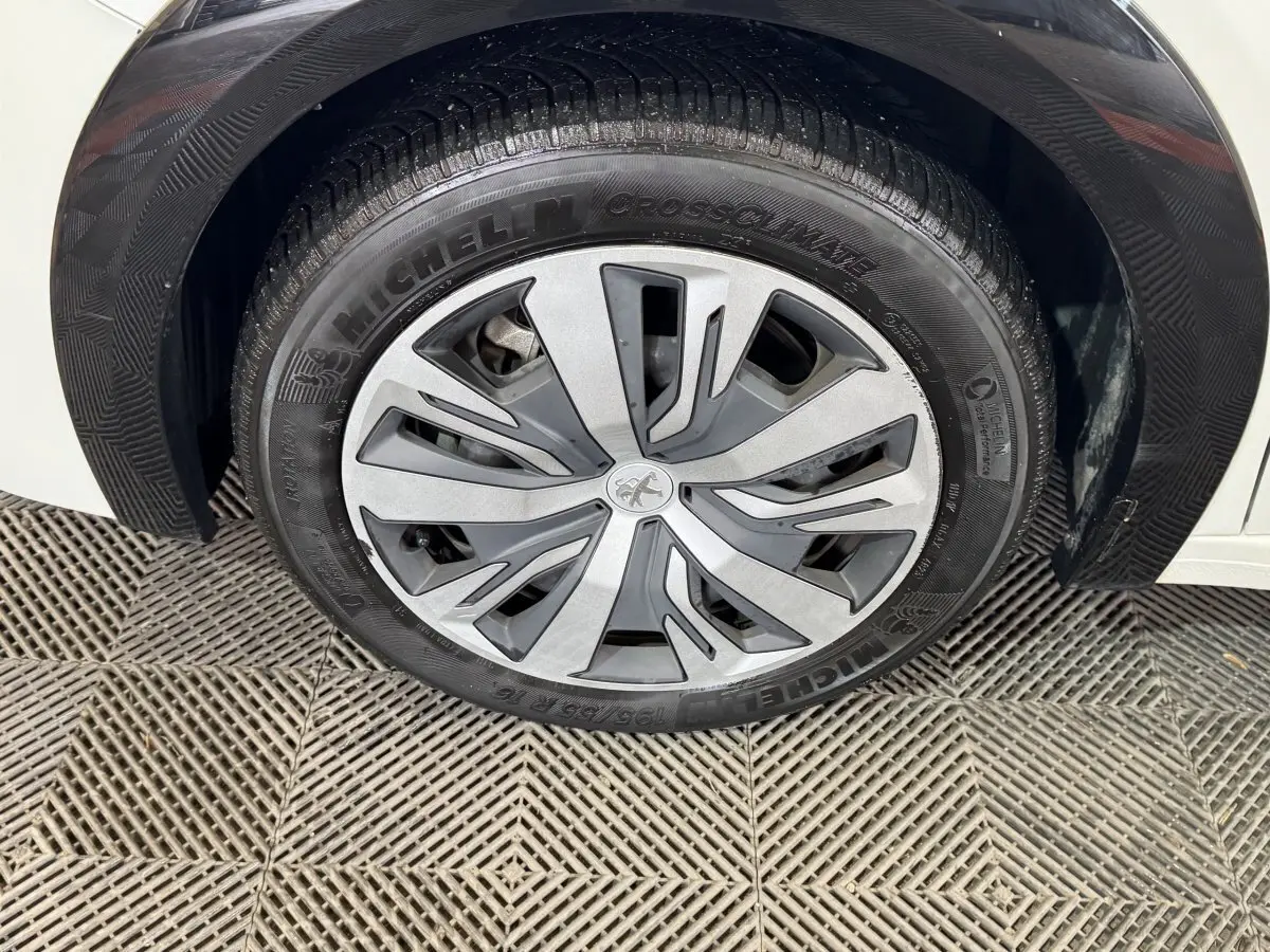 Gros plan sur la roue avant droite de la Peugeot 208 Electrique Active Business blanche, jante avec logo lion central.