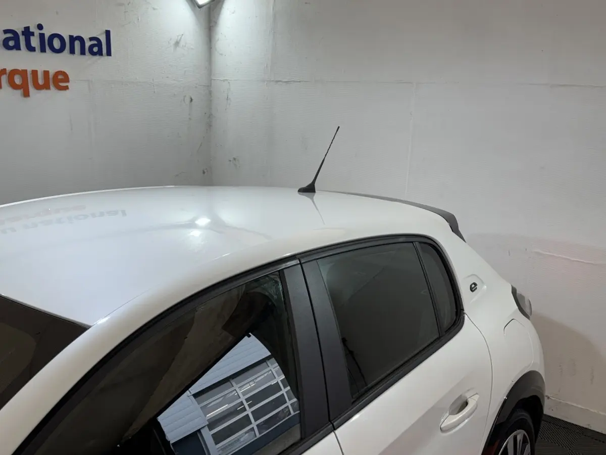 Vue partielle côté droit arrière d'une Peugeot 208 Electrique Active Business blanche, avec antenne de toit et vitres teintées.