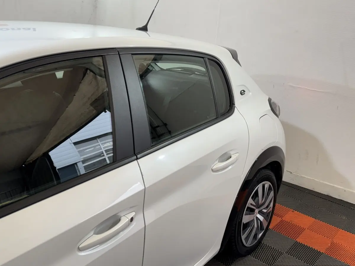 Vue 3/4 arrière droite d’une Peugeot 208 électrique blanche avec logo « e » sur l’aile arrière et jantes spécifiques.