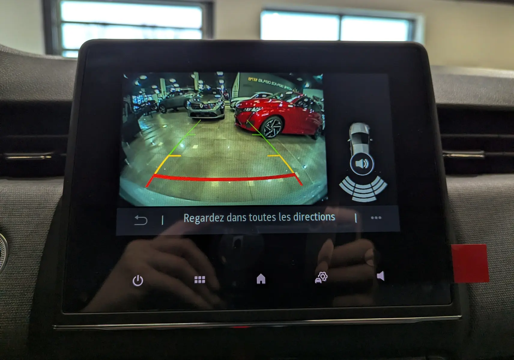 Écran central montrant la caméra de recul avec vue arrière sur un véhicule rouge et un autre gris dans un showroom.