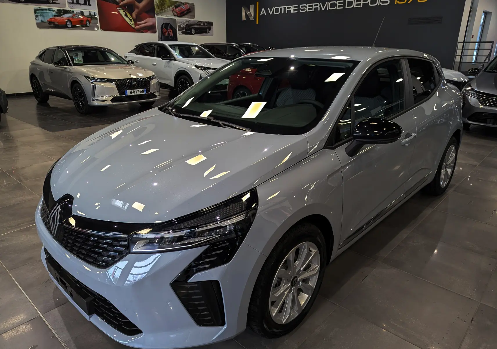 Renault Clio V Gris Rafale vue 3/4 avant droit en showroom, avec calandre noire et phares LED distinctifs.