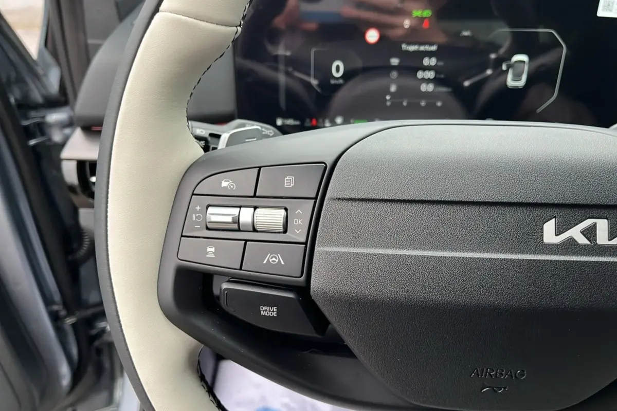 Gros plan sur le volant cuir clair du Kia Sportage 2026 avec commandes multifonctions et tableau de bord numérique flou.