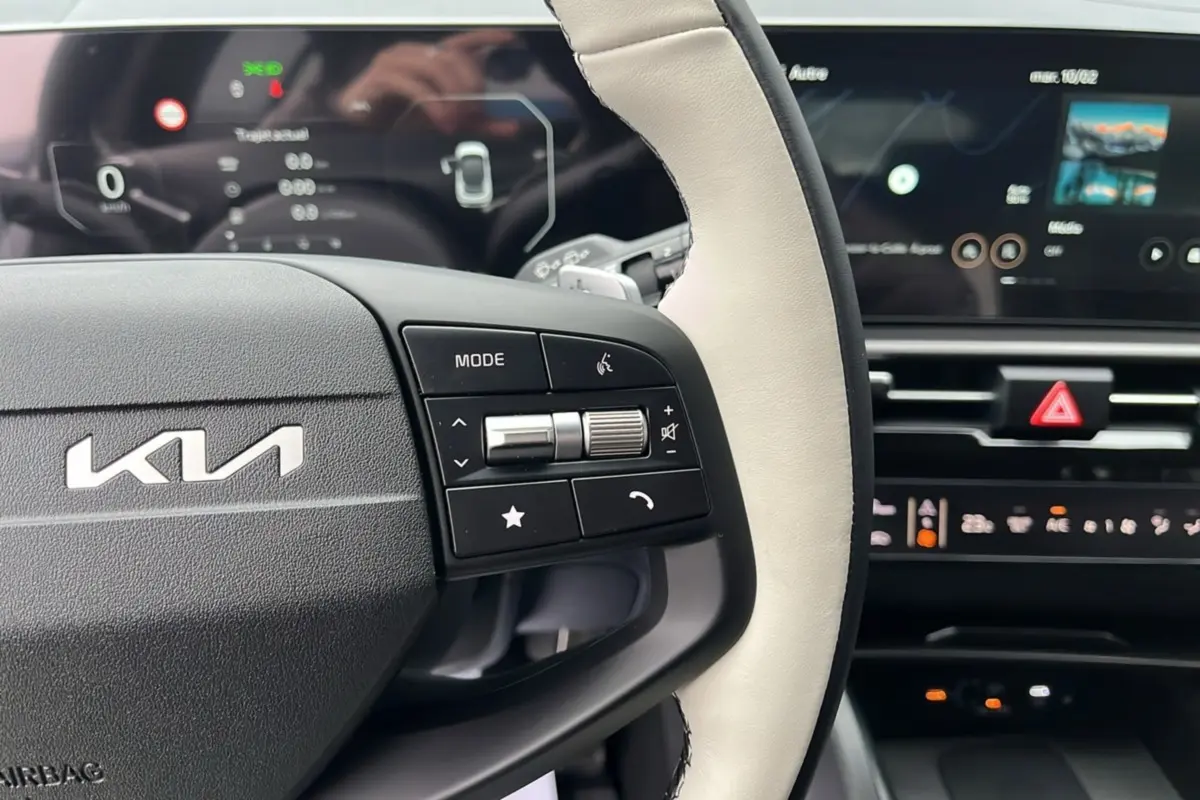 Vue rapprochée du volant cuir bicolore avec commandes multifonctions du Kia Sportage 2026, tableau de bord numérique en arrière-plan.