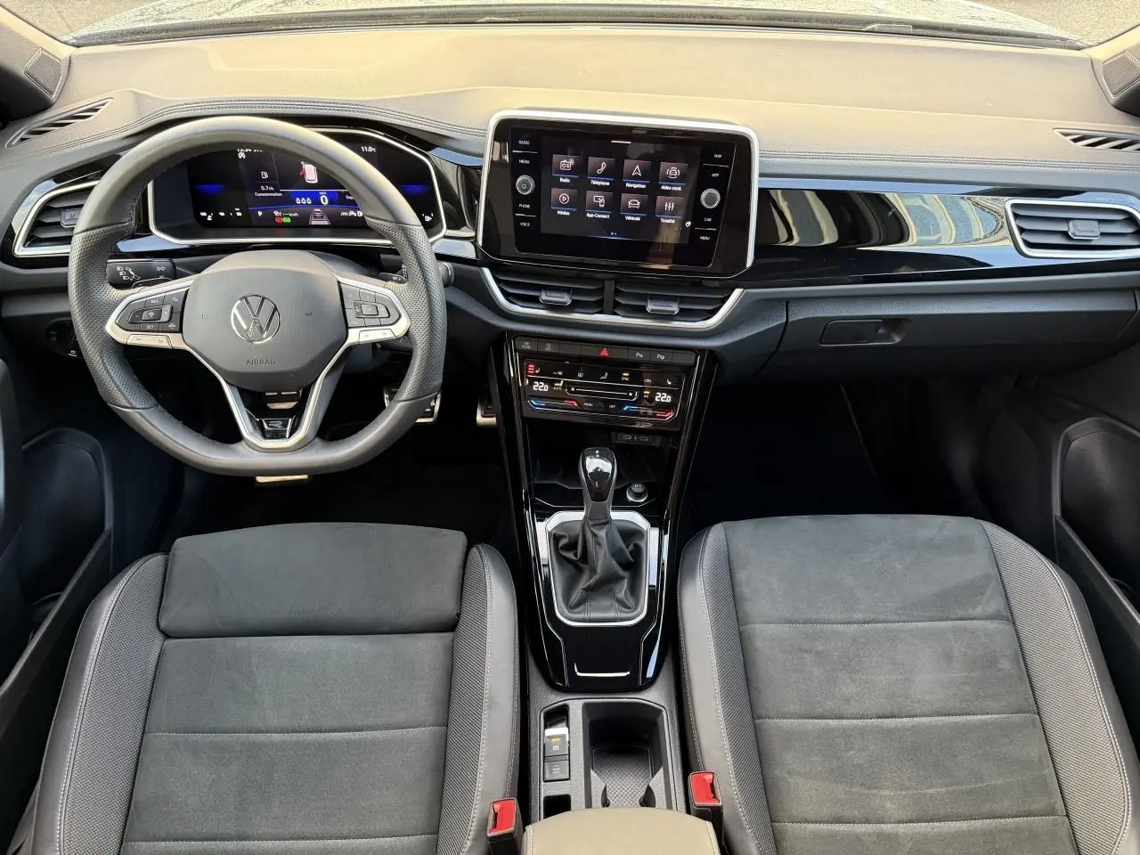 Vue intérieure avant du Volkswagen T-Roc 2025 avec tableau de bord noir, volant multifonction et console centrale avec boîte manuelle.