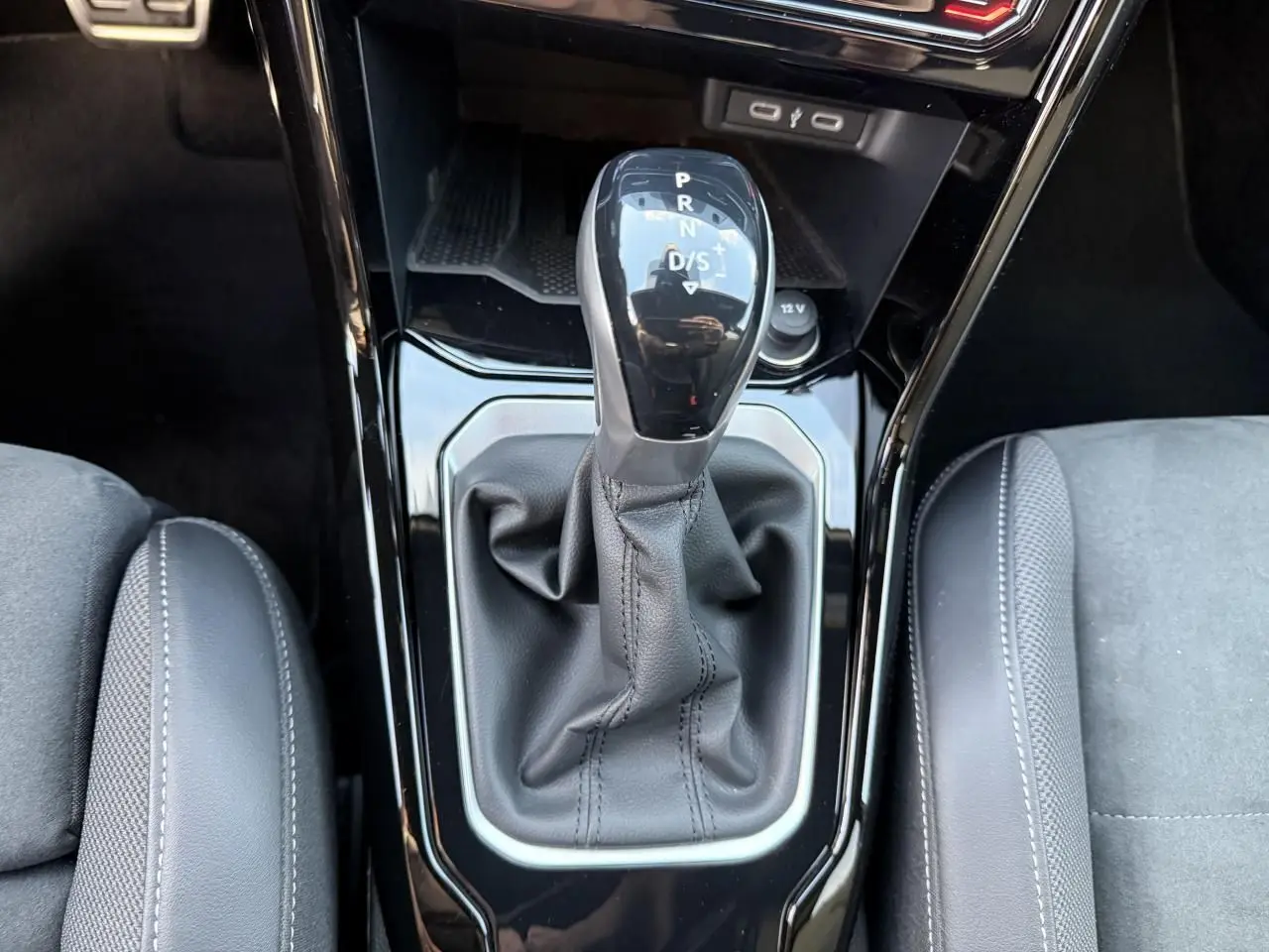 Gros plan sur le levier de vitesse manuel noir entouré de cuir, entre les sièges avant gris du Volkswagen T-Roc 2025.