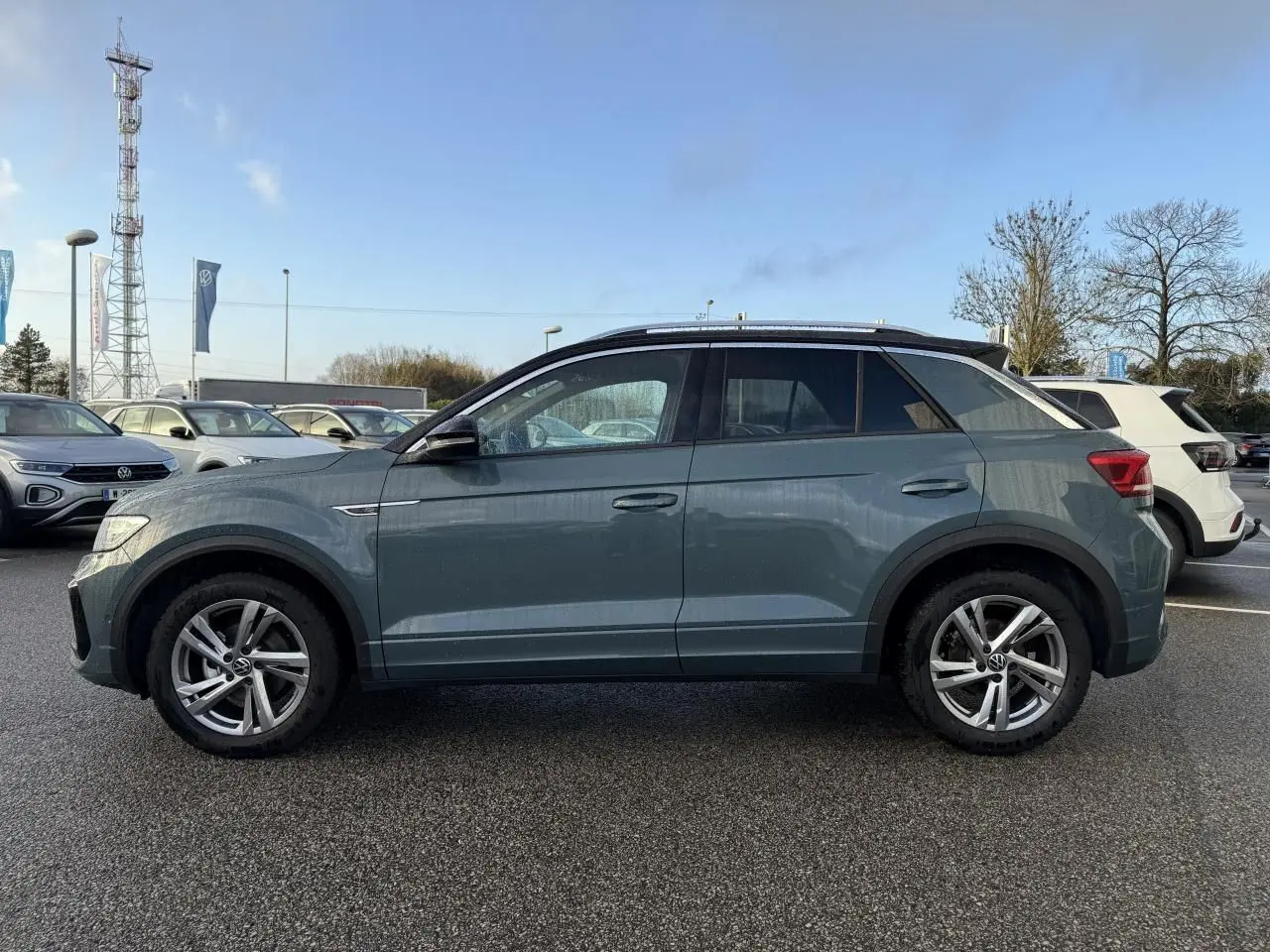 Vue de profil côté gauche d'un Volkswagen T-Roc bleu avec jantes alliage et barres de toit chromées.