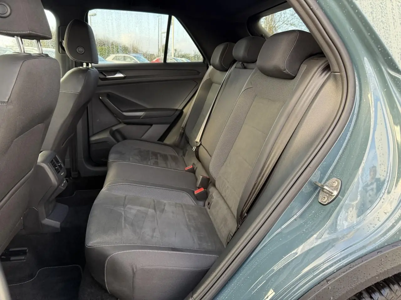 Vue côté droit de l'habitacle arrière du Volkswagen T-Roc 2025 bleu, sièges tissu et alcantara noirs avec ceintures de sécurité.