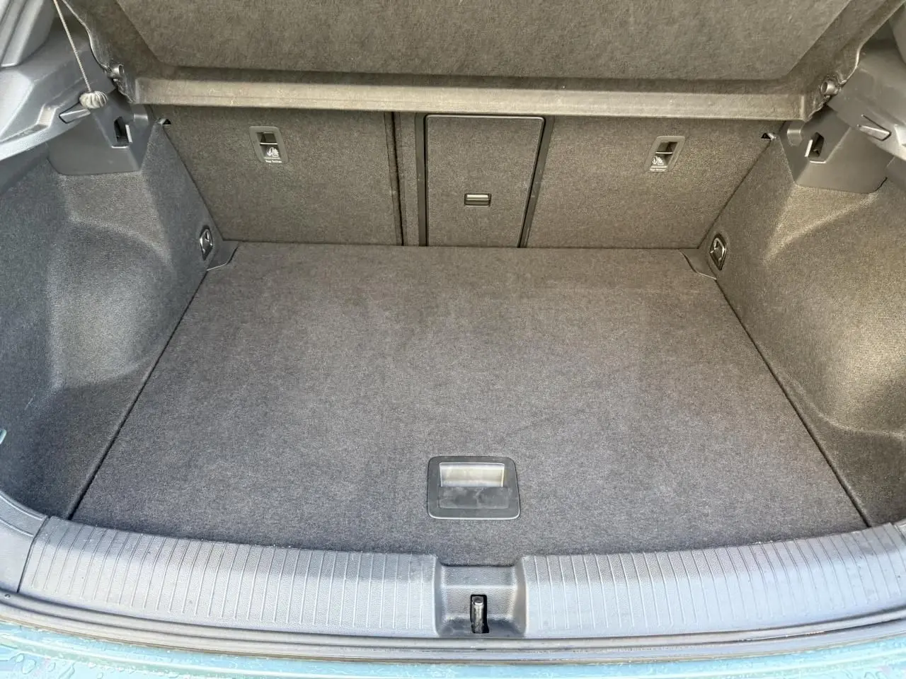 Coffre ouvert du Volkswagen T-Roc bleu, vue plongeante sur l'espace de chargement vide et tapis gris.