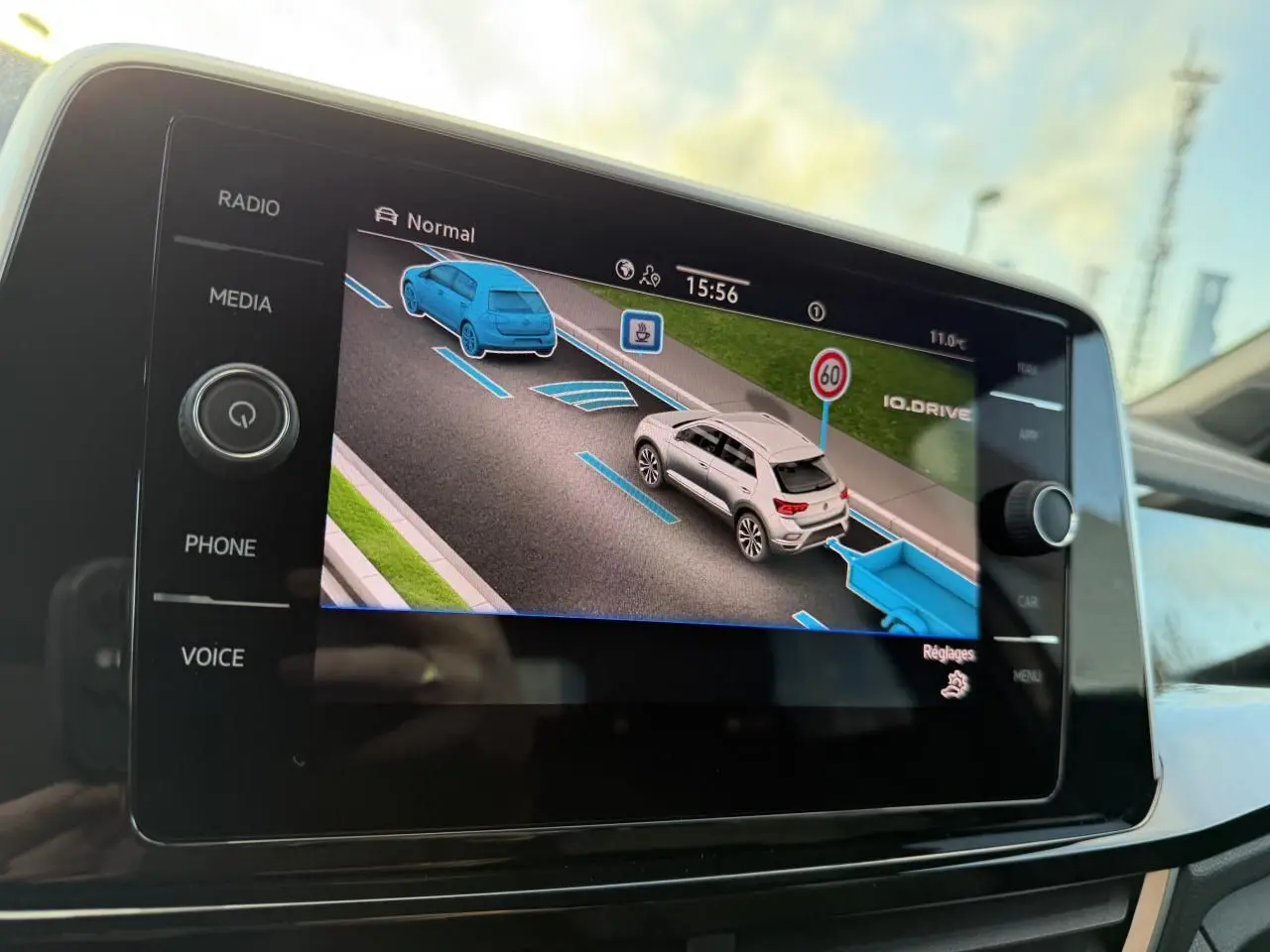 Écran tactile intérieur montrant l'assistance IQ.DRIVE avec vue 3D de deux véhicules sur route et panneau 60 km/h.