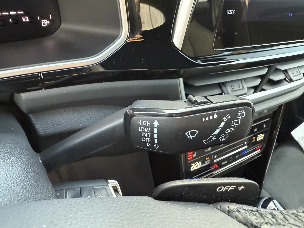 Gros plan sur la commande d’essuie-glace noire dans l’habitacle du Volkswagen T-Roc bleu, avec tableau de bord et climatisation tactile visibles.