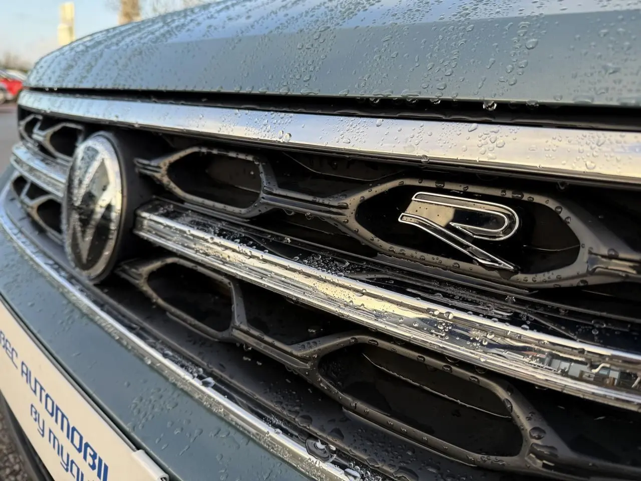 Gros plan sur la calandre avant bleue du Volkswagen T-Roc 2025 avec logo R et gouttes d'eau visibles.