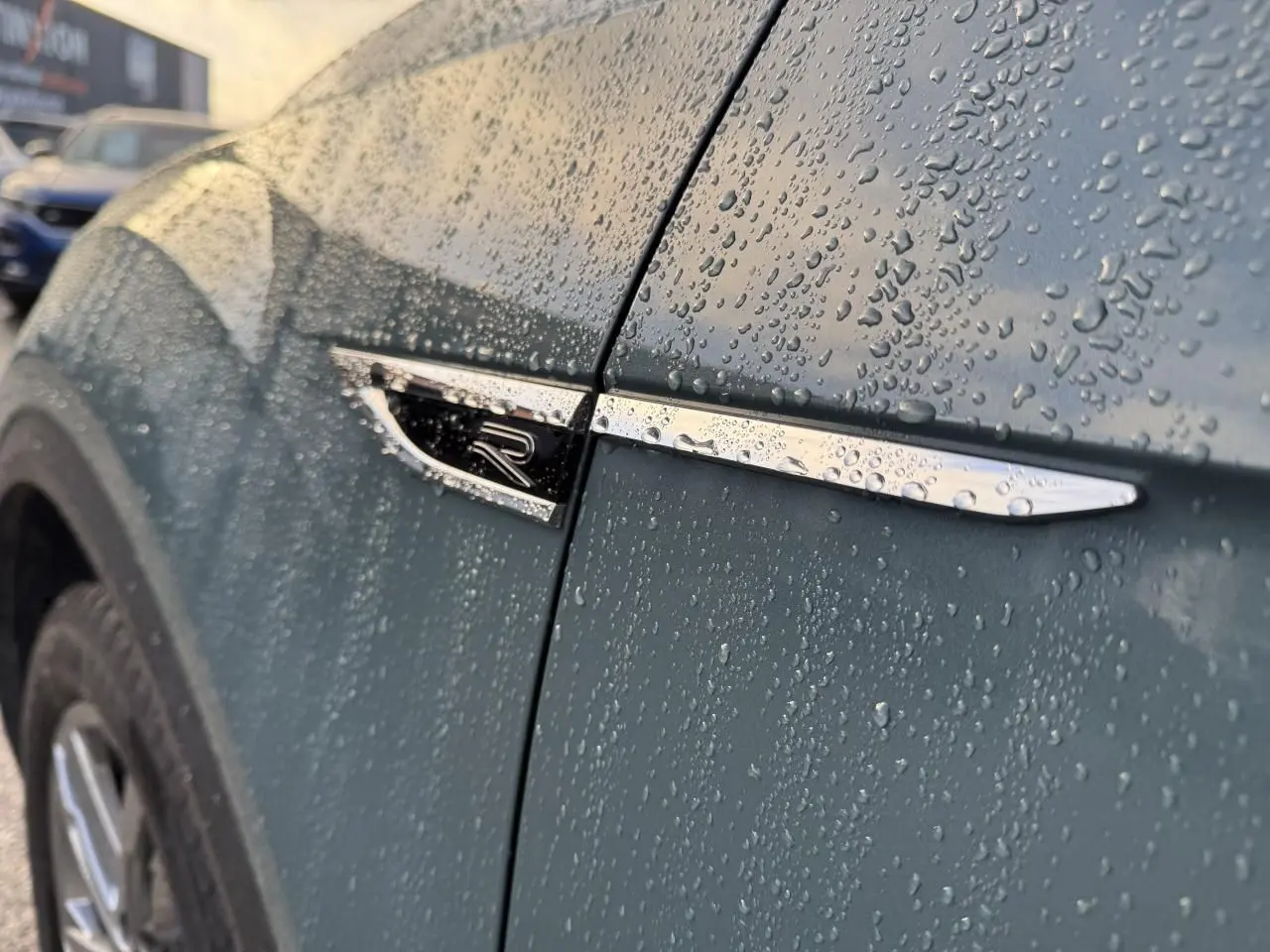 Détail de l'aile avant gauche bleu métallisé du Volkswagen T-Roc avec logo R sous la pluie.