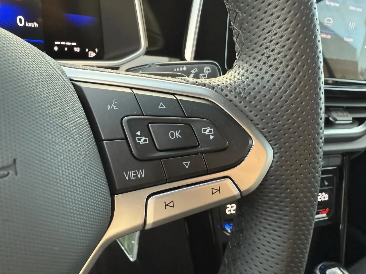 Gros plan sur le volant perforé noir du Volkswagen T-Roc 2025 avec commandes multifonctions et écran digital en arrière-plan.