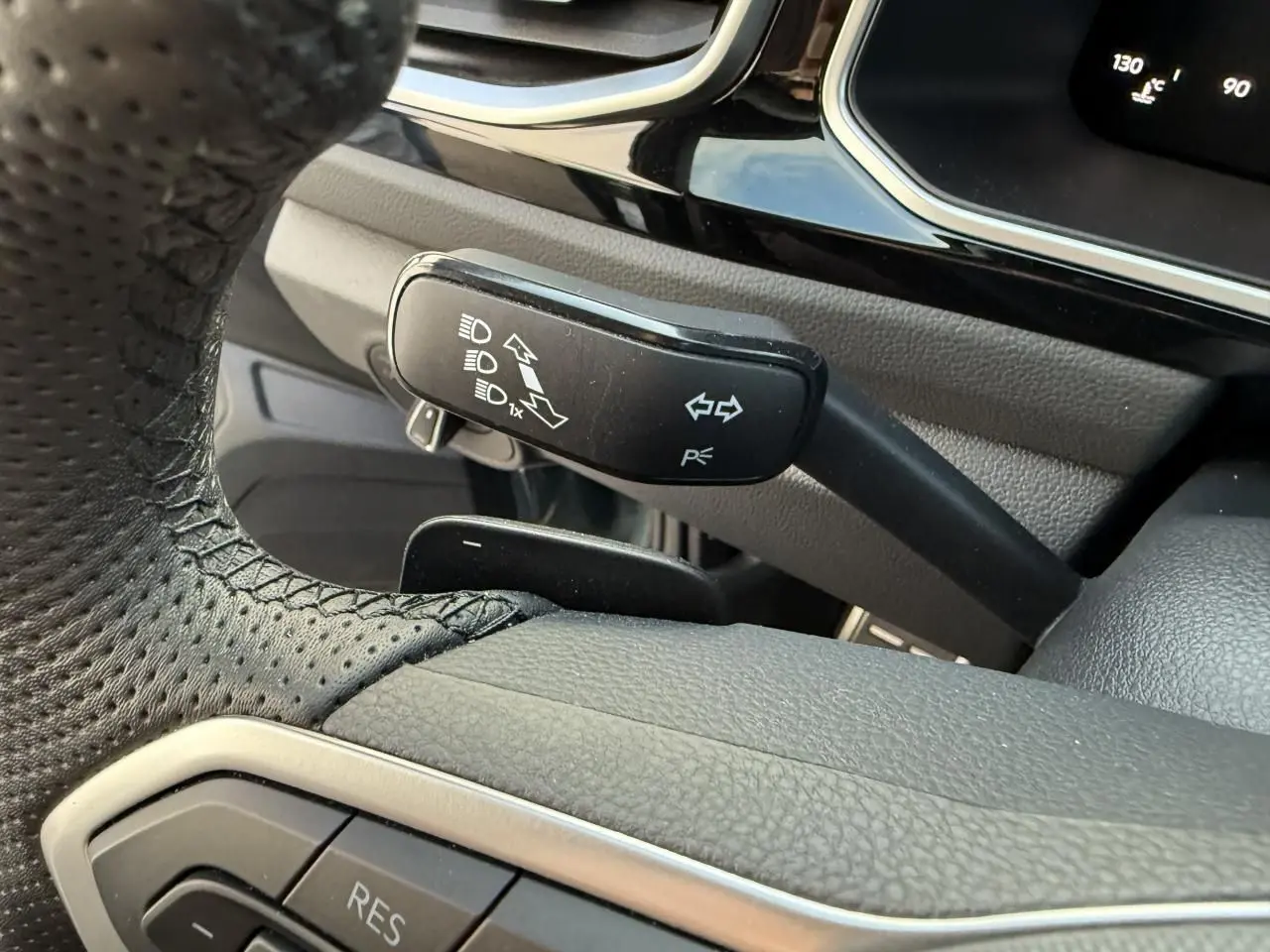 Gros plan sur la manette de clignotants noire à gauche du volant perforé du Volkswagen T-Roc bleu 2025.