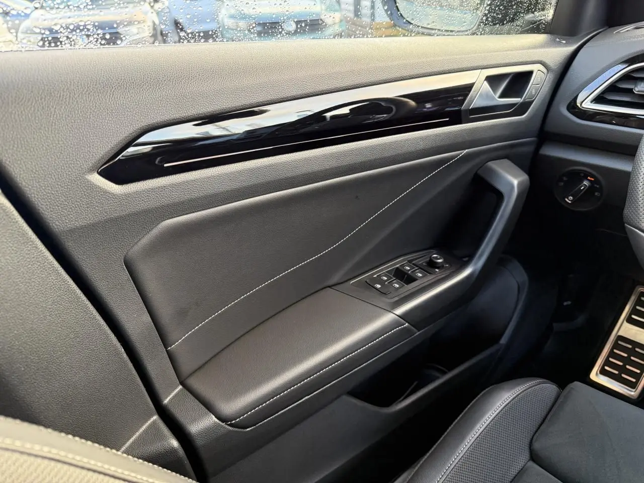 Vue intérieure côté gauche de la porte avant d’un Volkswagen T-Roc bleu, avec garniture noire et commandes électriques.