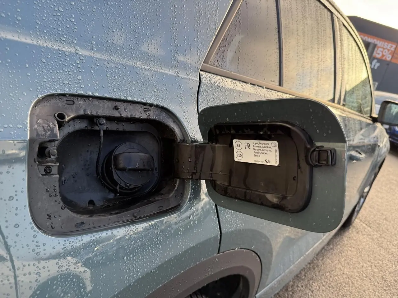 Vue rapprochée de la trappe à carburant ouverte côté gauche d’un Volkswagen T-Roc bleu avec gouttes d’eau.