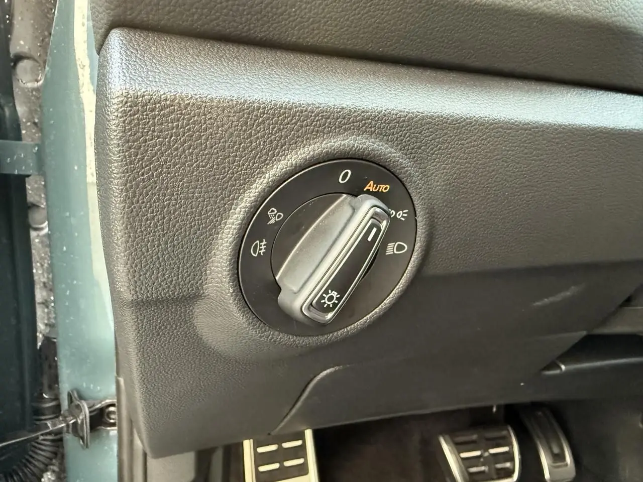 Gros plan sur la commande des feux et pédalier en acier inoxydable dans l'habitacle noir du Volkswagen T-Roc bleu.