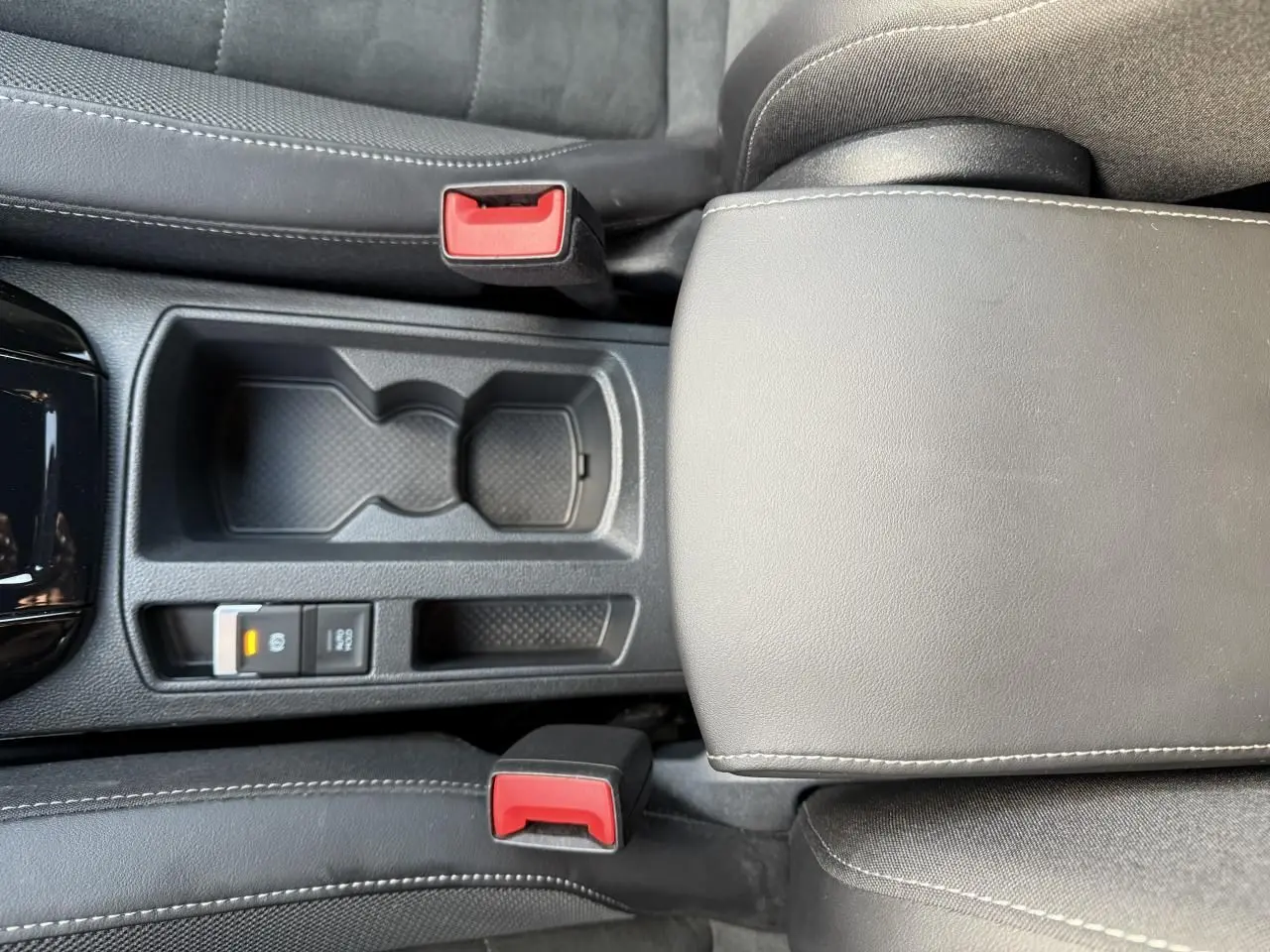 Vue plongeante sur la console centrale noire du Volkswagen T-Roc 2025, avec accoudoir et boutons de frein de stationnement.