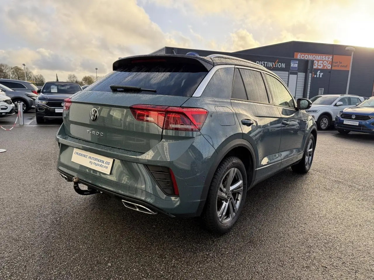 Vue 3/4 arrière droite d'un Volkswagen T-Roc bleu avec attelage amovible et jantes alliage gris galvanisé.