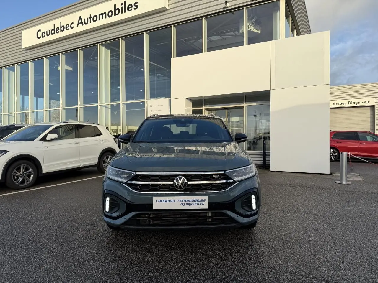 Vue avant d'un Volkswagen T-Roc bleu garé devant un concessionnaire avec calandre et feux LED visibles.