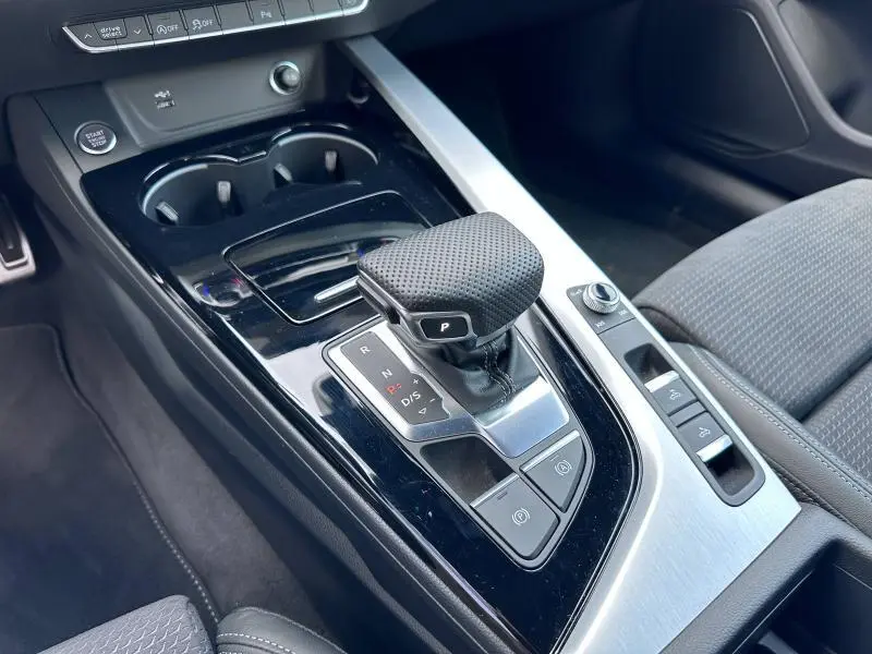Gros plan sur la console centrale noire brillante de l'Audi A5 Cabriolet 2023 avec levier de vitesses automatique et sièges gris.