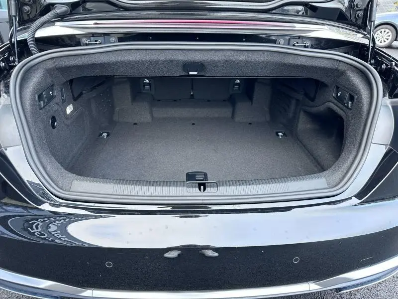 Coffre ouvert vu de face de l'Audi A5 Cabriolet noir brillant, montrant un espace de rangement propre et spacieux.