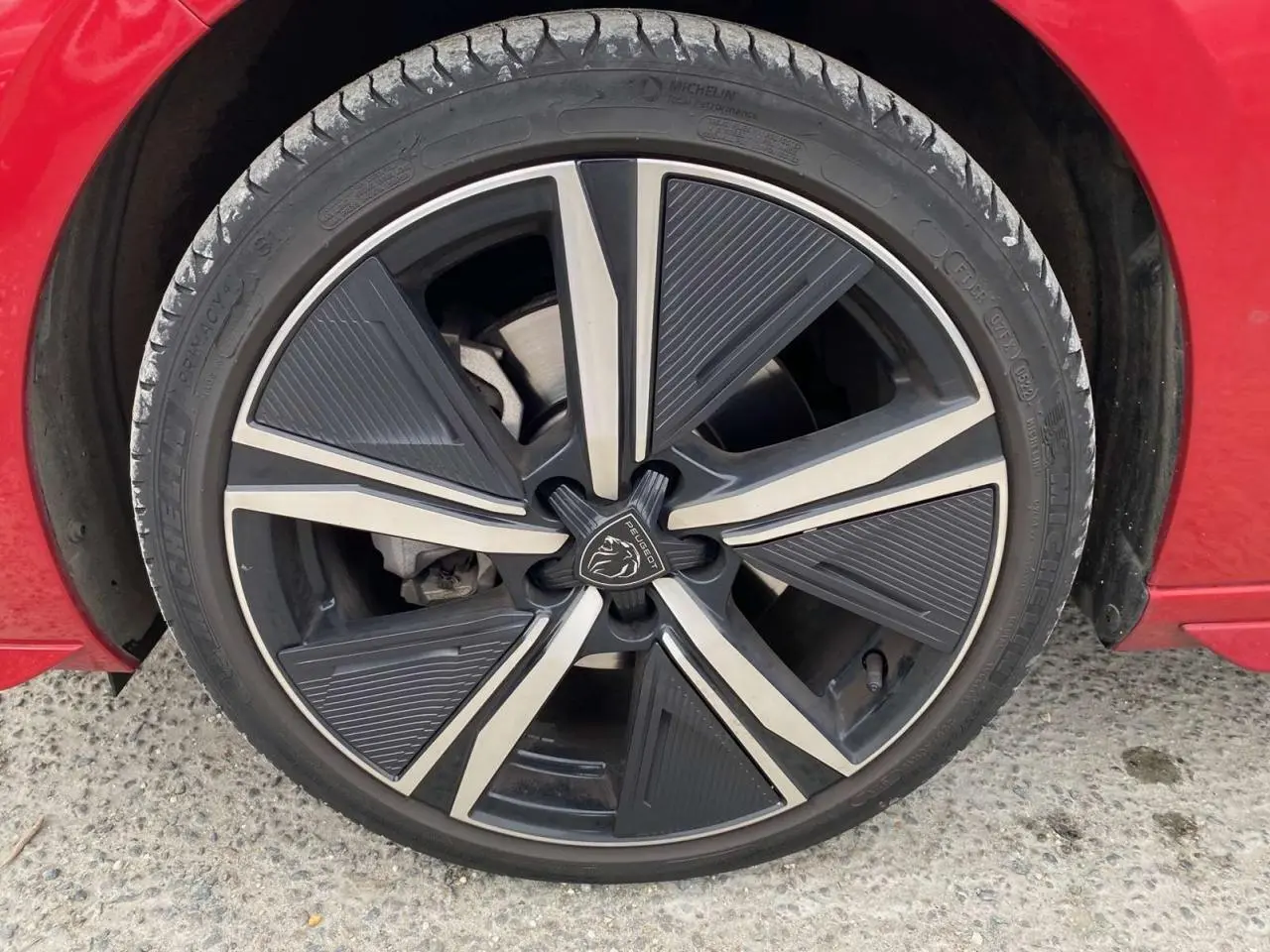 Gros plan sur la roue avant gauche d'une Peugeot 308 rouge Elixir avec jante alliage au design moderne.