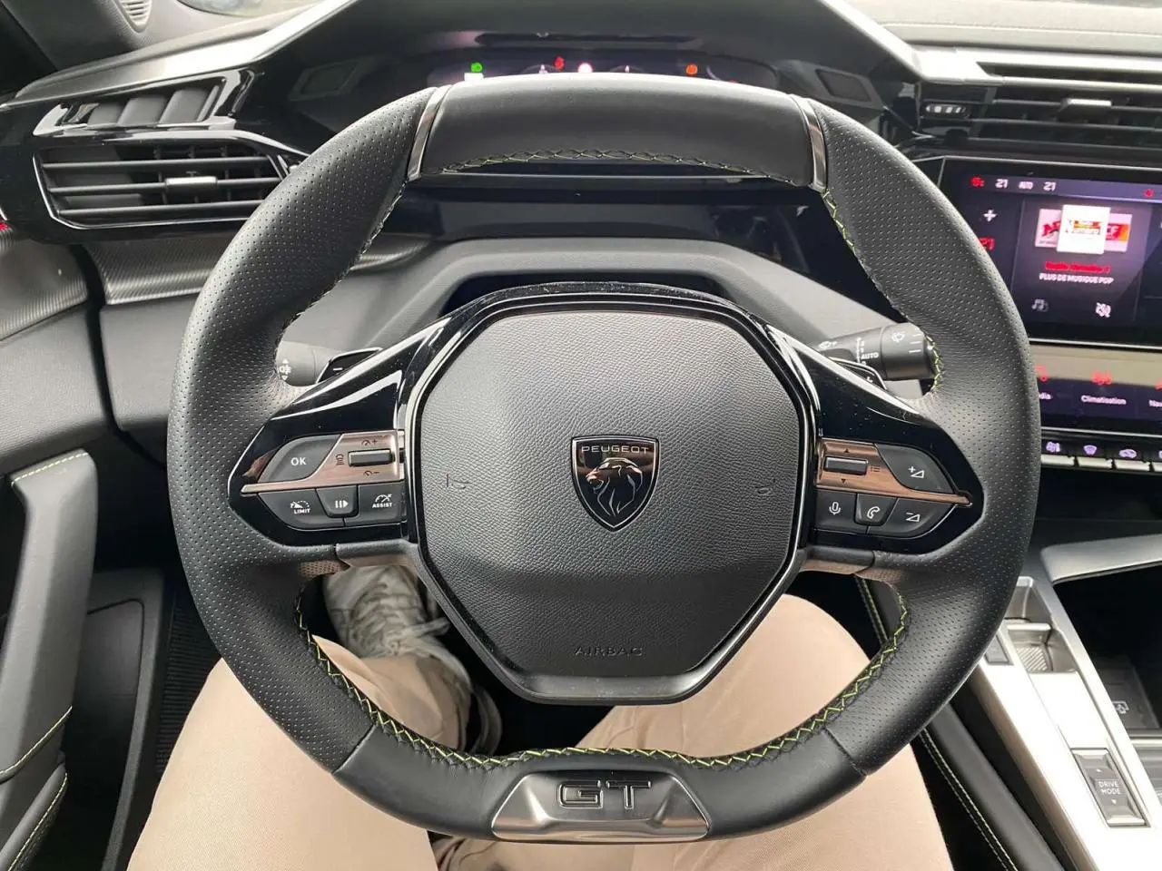 Vue rapprochée du volant GT noir avec surpiqûres vertes du Peugeot 308 Rouge Elixir, tableau de bord et écran tactile visibles.