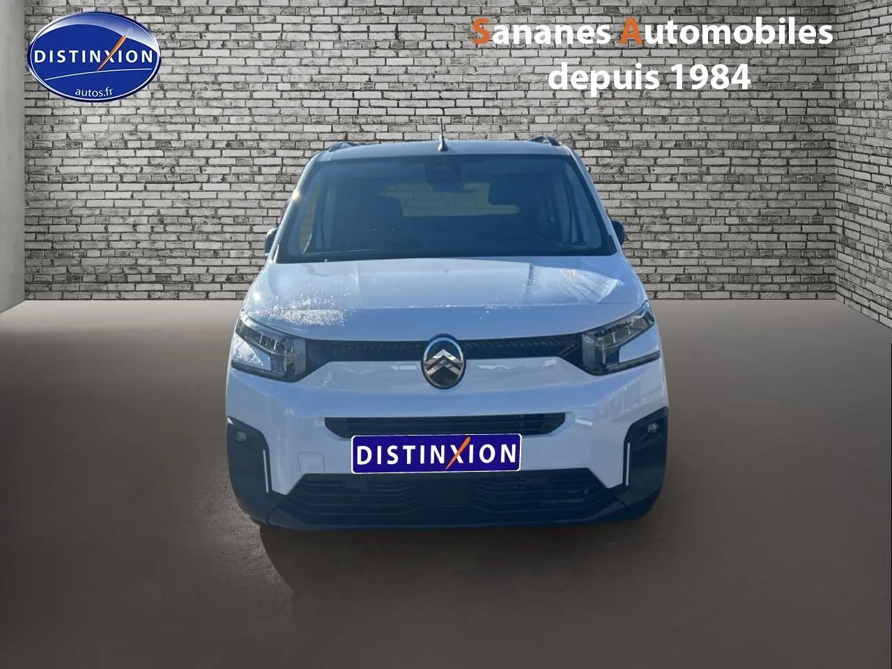 Vue frontale d'un Citroën Berlingo blanc 2025 avec logo chromé et pare-chocs noir dans un décor brique.