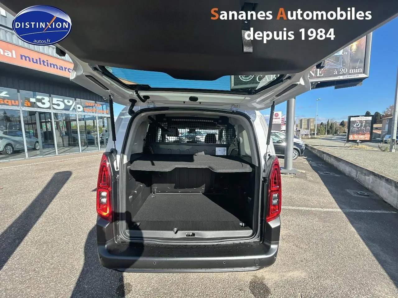 Vue arrière ouverte du Citroën Berlingo blanc montrant le coffre spacieux et la grille de séparation intérieure.