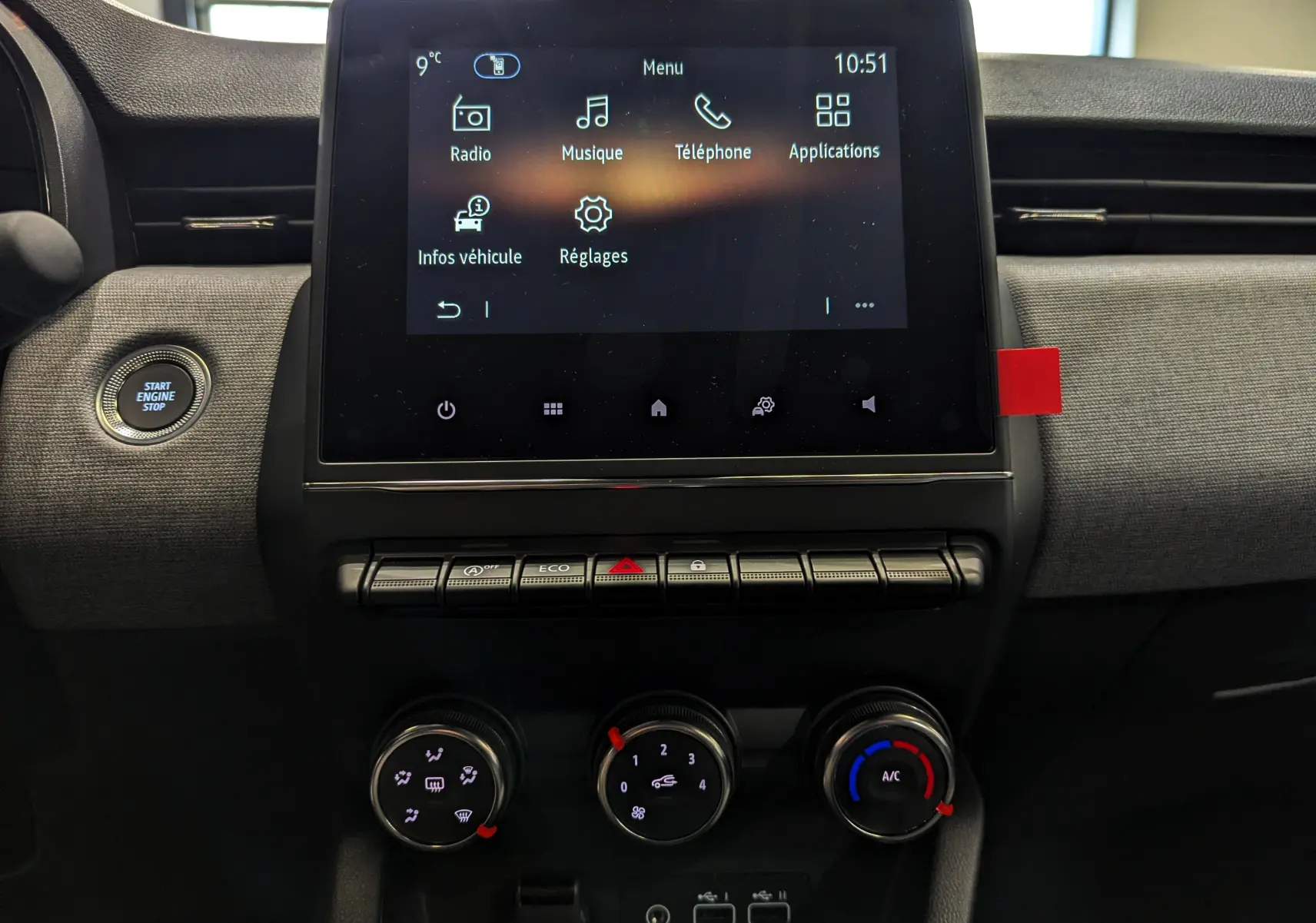 Vue rapprochée de la console centrale de la Renault Clio V gris Rafale, avec écran tactile et commandes de climatisation.