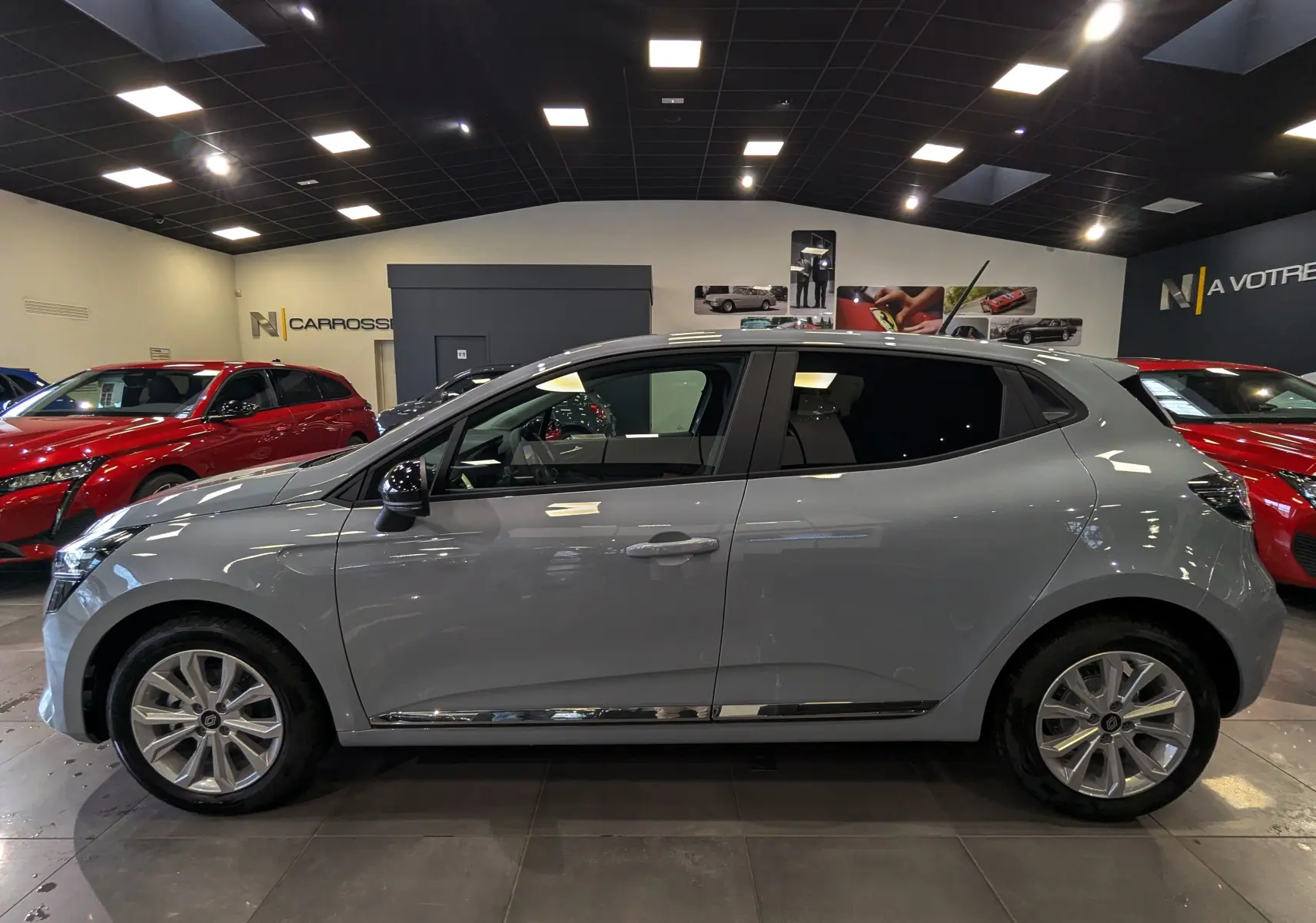 Renault Clio V gris Rafale vue de profil côté gauche, en intérieur avec jantes alliage et vitres teintées.