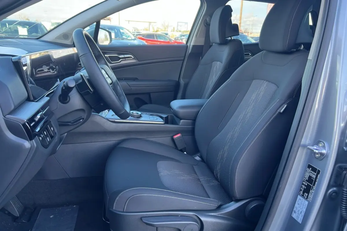 Vue intérieure côté conducteur du Kia Sportage gris perle 2026, sièges tissu noirs avec console centrale et volant multifonctions.