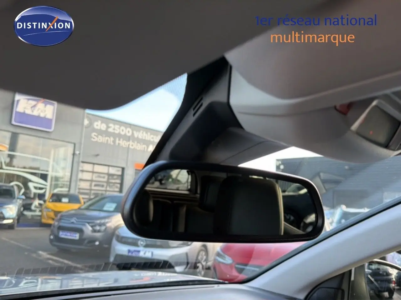 Vue intérieure centrée sur le rétroviseur intérieur d’un Citroën C5 Aircross gris Artense, avec parking en arrière-plan.