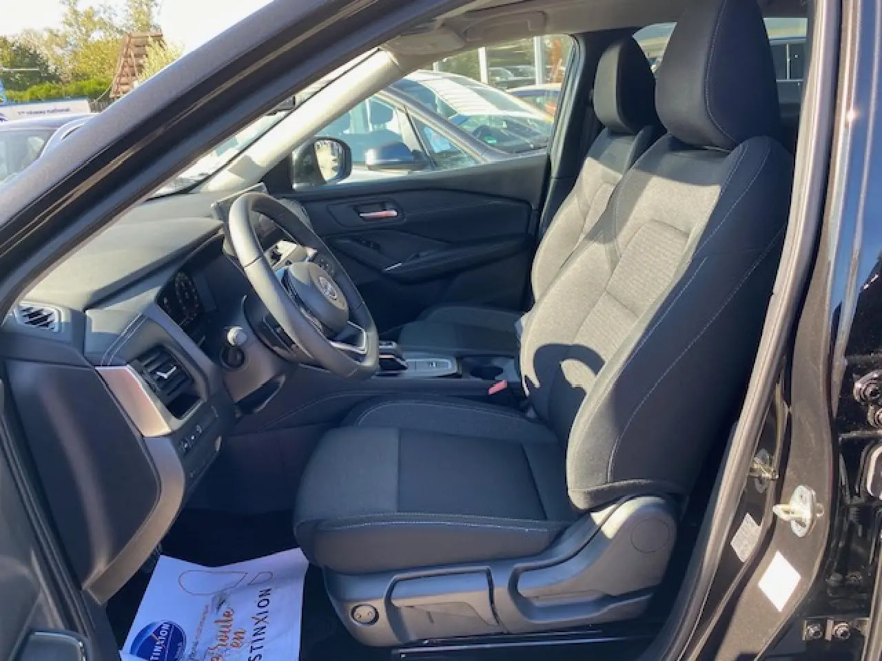 Intérieur côté conducteur du Nissan Qashqai noir 2023, montrant sièges en tissu et tableau de bord moderne.