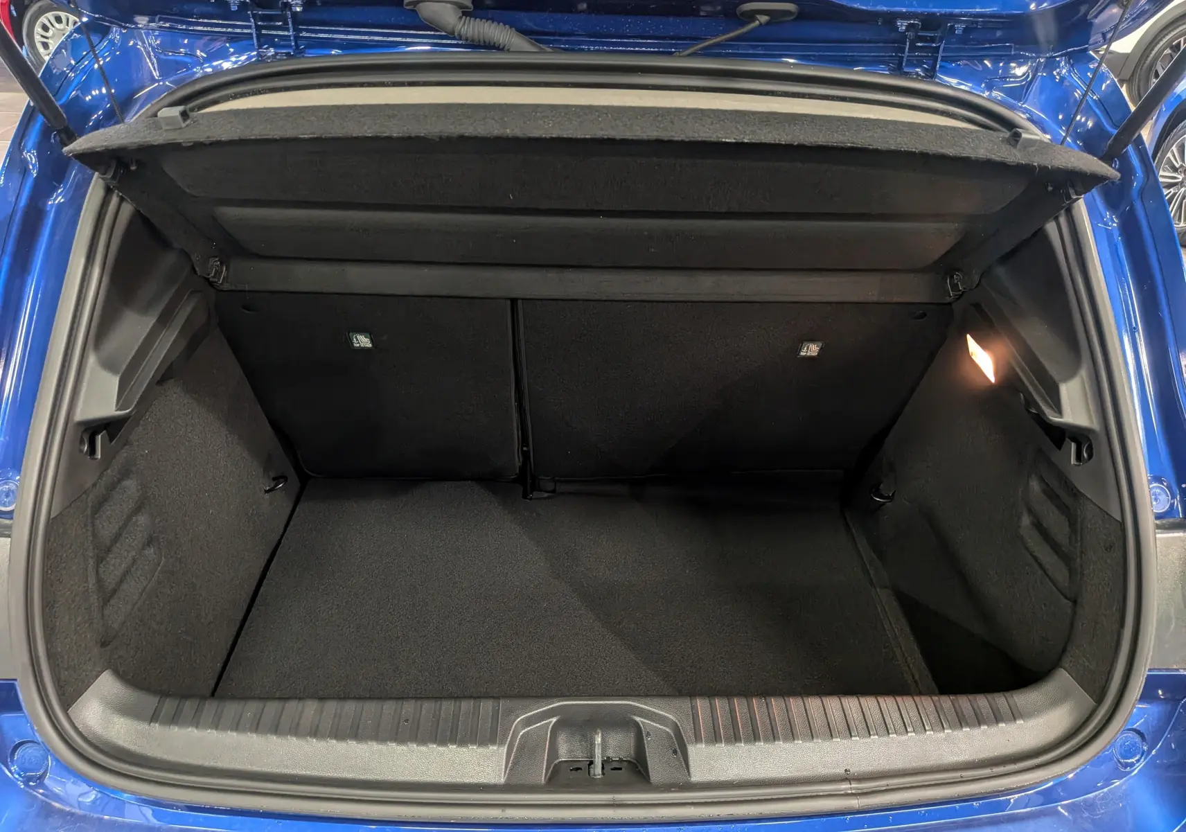 Coffre ouvert vu de l'arrière d'une Renault Clio V Bleu Iron, montrant l'espace de rangement vide et l'éclairage intérieur.