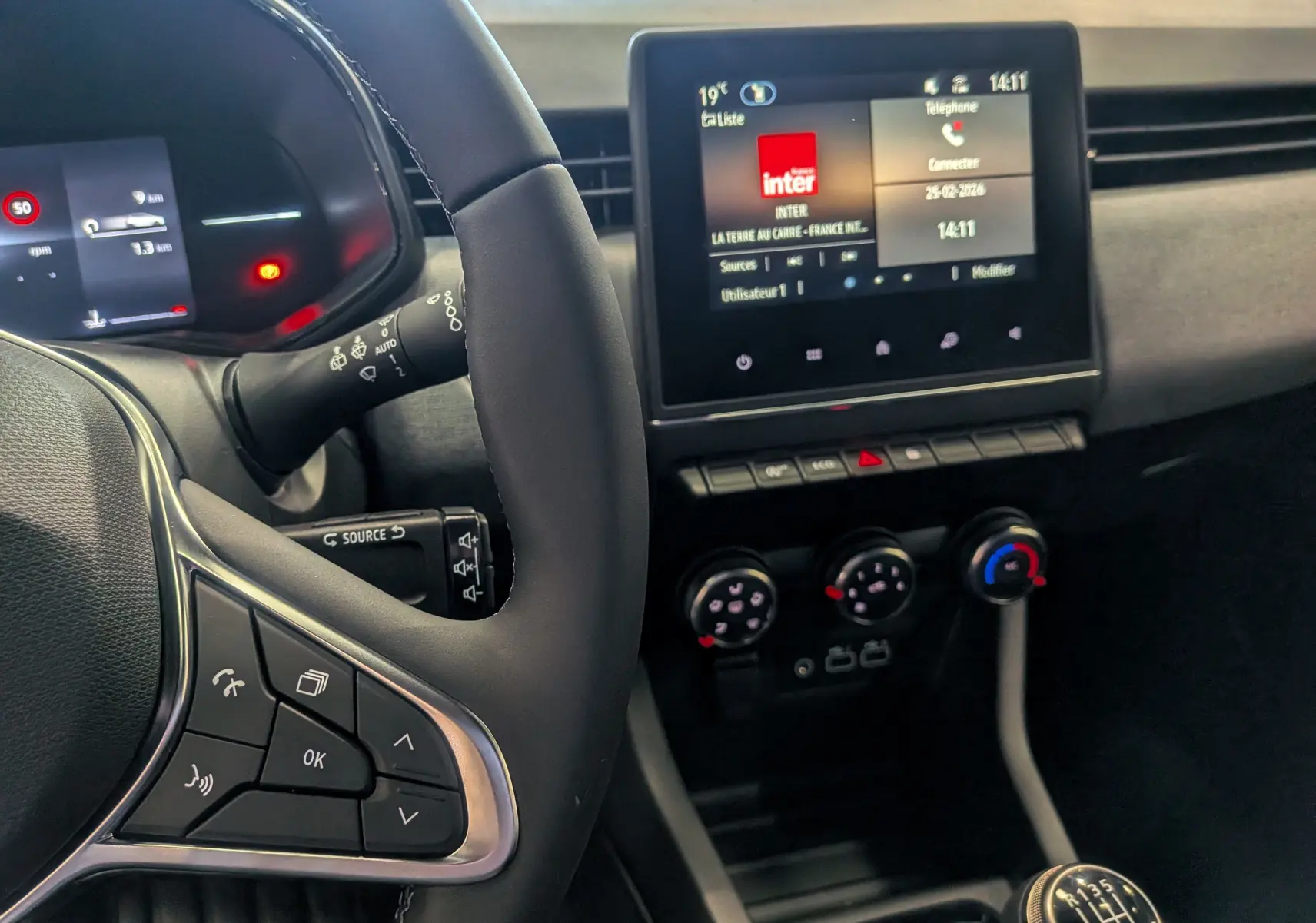 Vue intérieure côté conducteur de la Renault Clio V Diesel 2025, avec volant, écran tactile et levier de vitesse manuel visible.