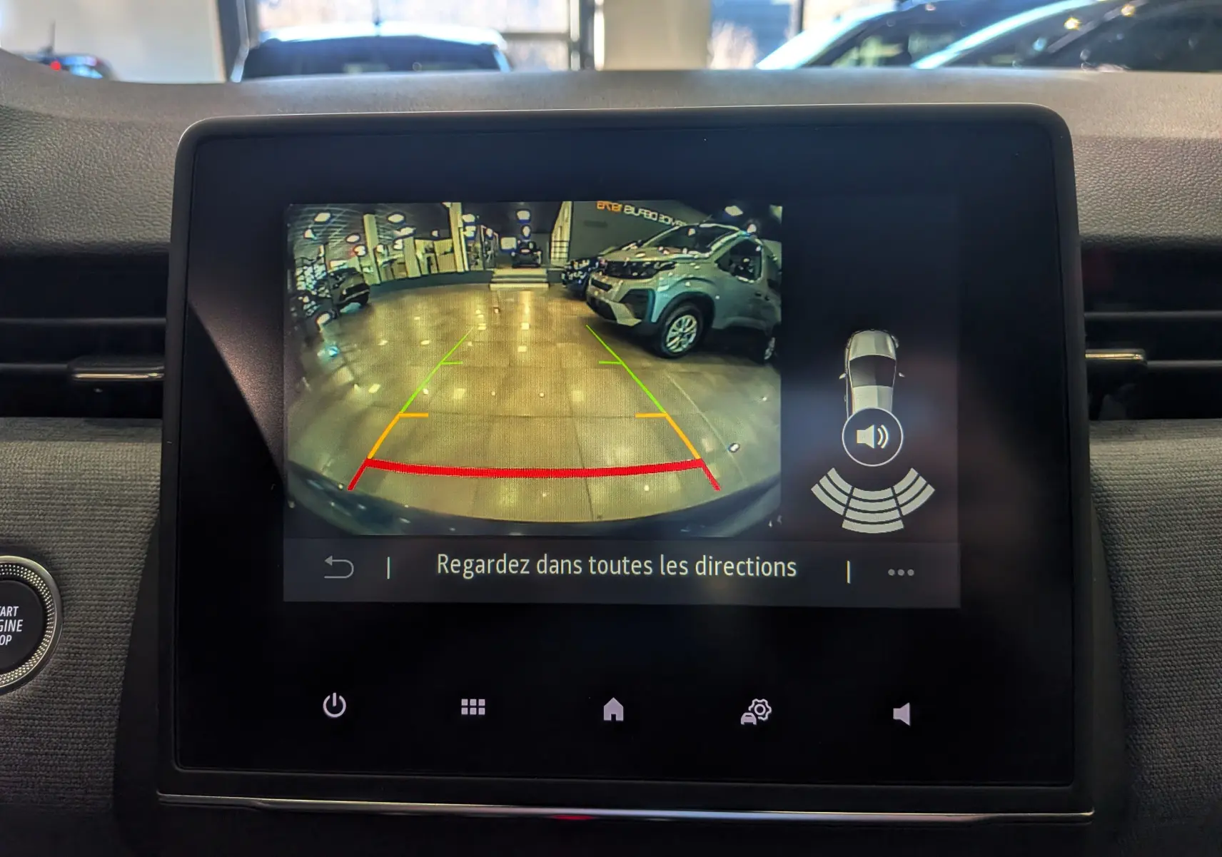 Écran de caméra de recul de la Renault Clio V bleu Iron montrant l’arrière en intérieur avec lignes de guidage colorées.