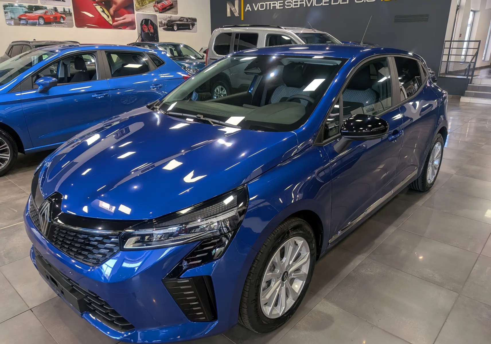 Renault Clio V Bleu Iron vue 3/4 avant droit en showroom, mettant en valeur ses optiques modernes et jantes argentées.