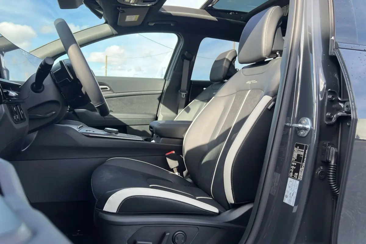 Vue intérieure côté conducteur du Kia Sportage 2026 gris eclipse avec sièges sport noirs et toit panoramique ouvert.