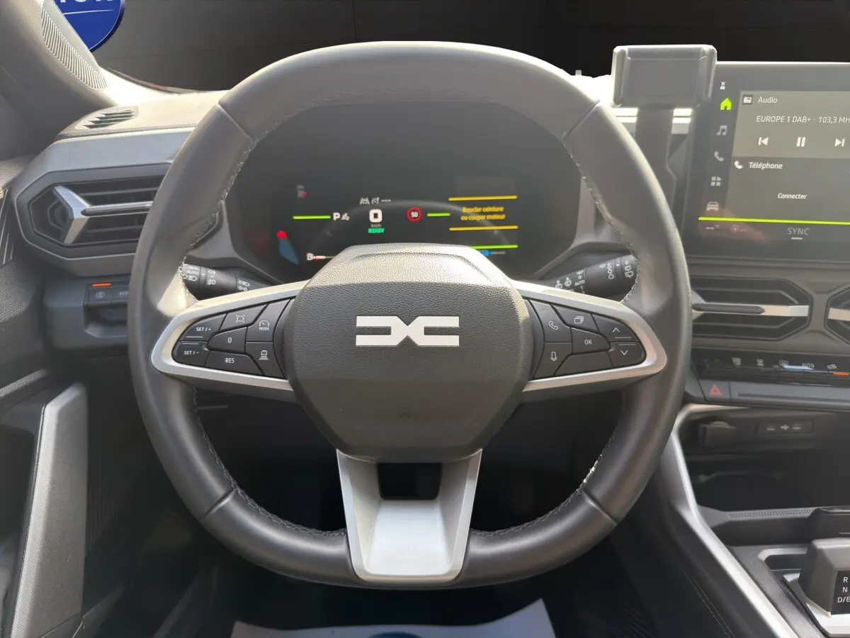 Vue intérieure centrée sur le volant cuir noir du Dacia Bigster Journey Hybrid 2025 avec tableau de bord numérique et écran tactile.