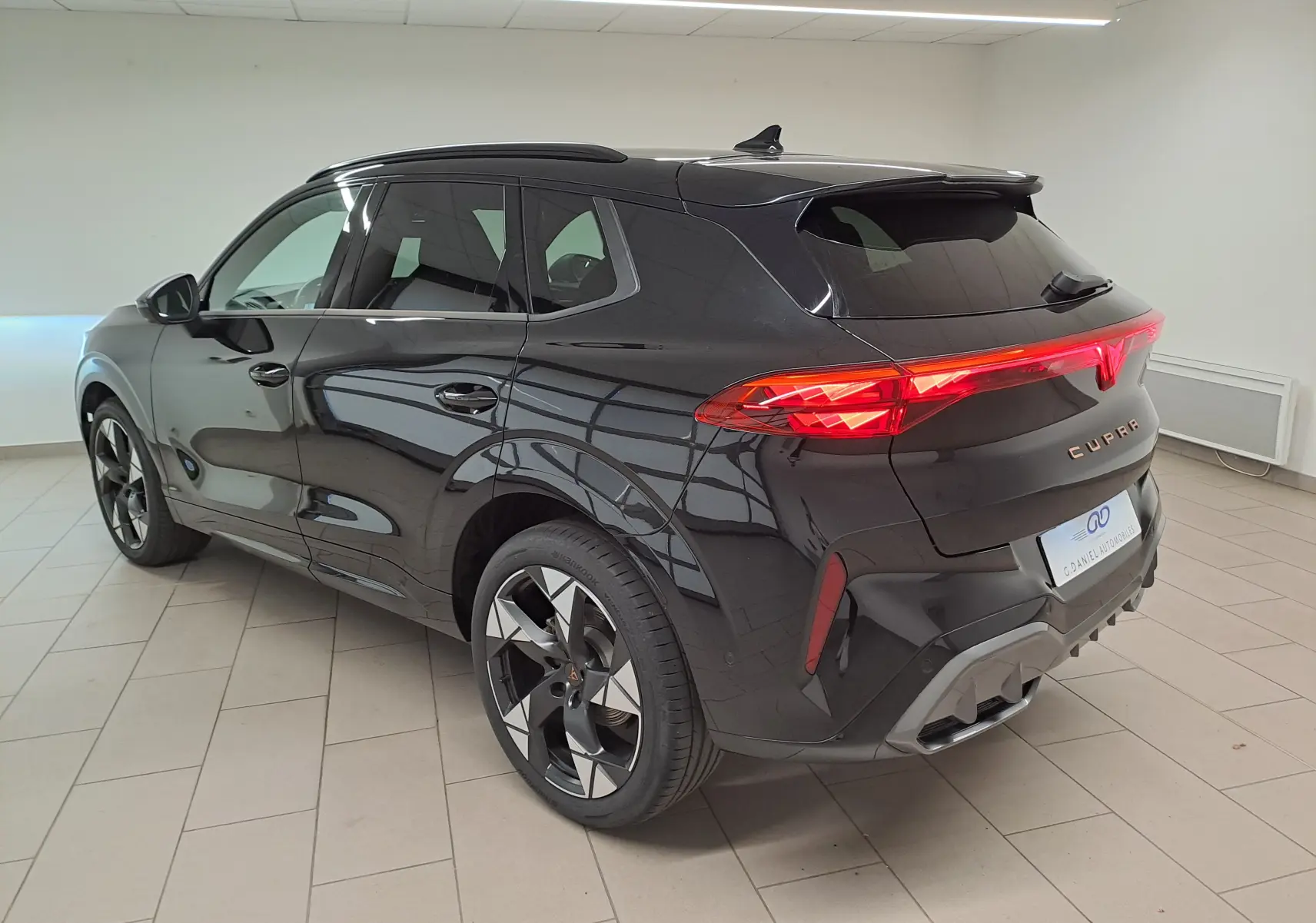 Vue 3/4 arrière droite du CUPRA TERRAMAR noir minuit avec jantes 20'' Gravity et feux arrière allumés en intérieur.